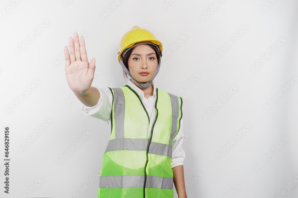 Serious Asian woman labor wearing safety helmet and vest with hand gesture pose rejection or prohibition, isolated by white background