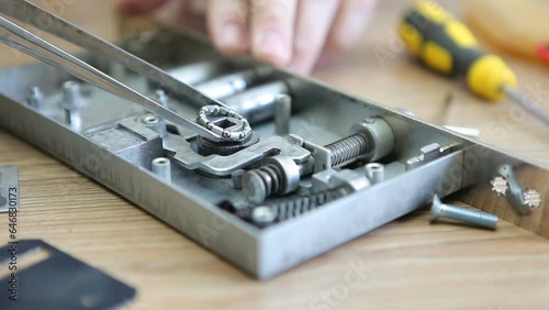 A man disassembles and repairs an internal door lock, removes the bearing with tweezers. Macro photography. photo
