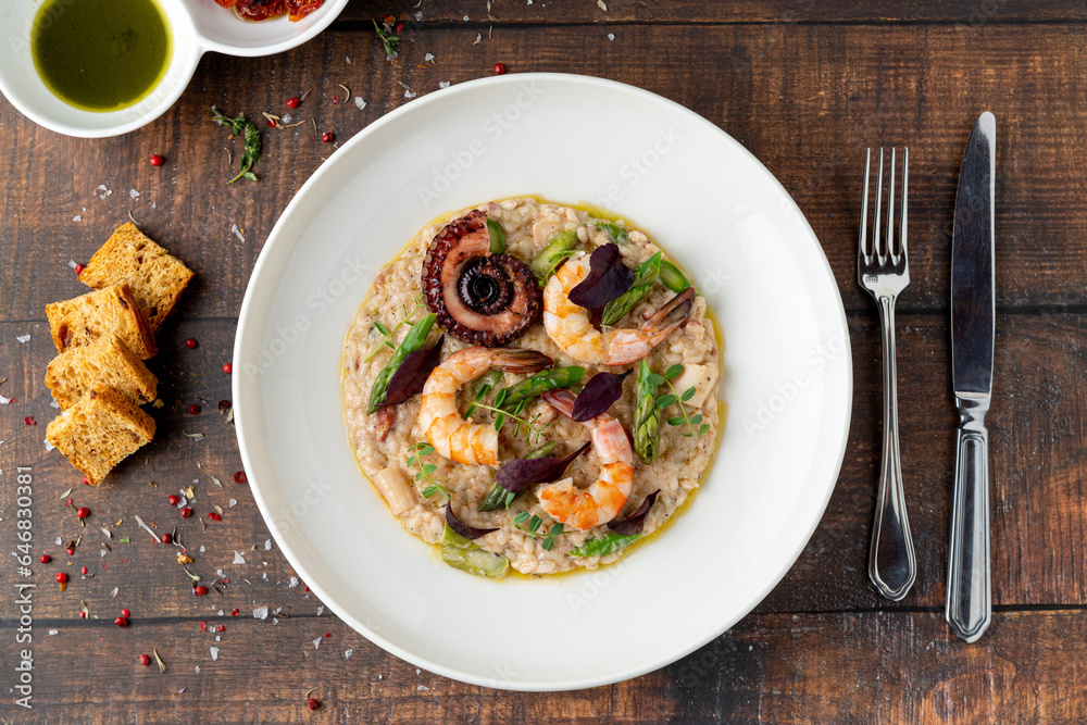 Risotto with jumbo shrimp and octopus on a white porcelain plate on wooden table. Seafood risotto Risotto with jumbo shrimp and octopus on a white porcelain plate on wooden table. Seafood risotto