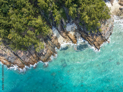 High angle aerial bird's eye drone view of the rocky coastline and tiny beaches on Arkhurst Island, a small islet near Hayman Island, Whitsunday Islands, Great Barrier Reef, Queensland, Australia.