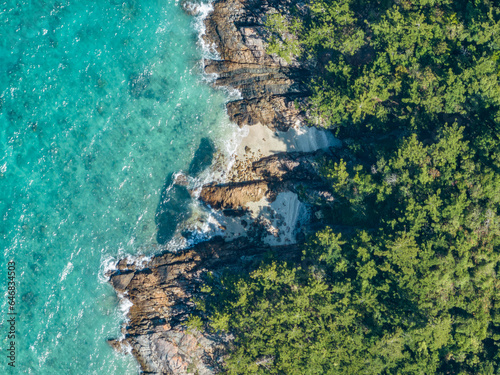 High angle aerial bird's eye drone view of the rocky coastline and tiny beaches on Arkhurst Island, a small islet near Hayman Island, Whitsunday Islands, Great Barrier Reef, Queensland, Australia.