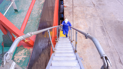 Fototapeta Naklejka Na Ścianę i Meble -  An engineer is walking up on the gangway accommodation ladder beside Oil tanker ship at harbor, view from above with copy space