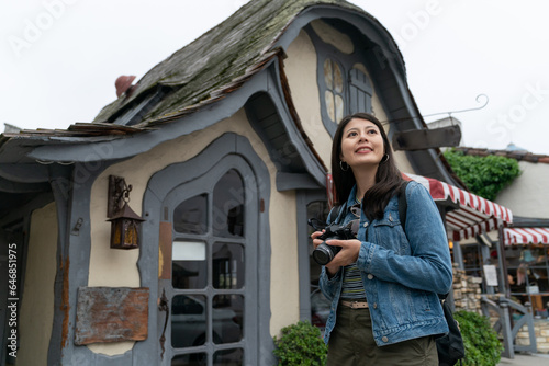 travel lifestyle and people in usa. low angle shot of asian girl visitor enjoying beautiful scenery with camera against background of a fairytale house building in Carmel by the sea