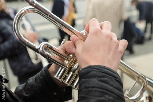 close-up of the hands of a street musician holding a gold-colored pump-action trumpet 