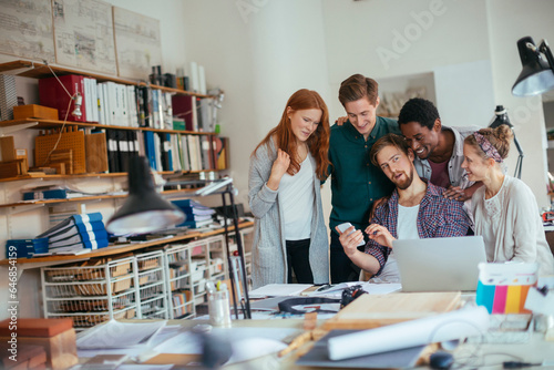 Young and diverse group of coworkers using a smartphone while working together on a project in a modern and contemporary business office