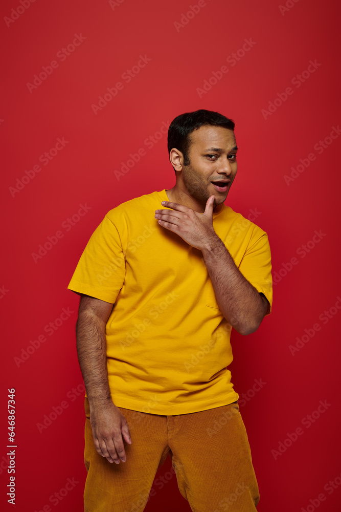 confidant indian man in bright casual clothes looking at camera and posing on red background