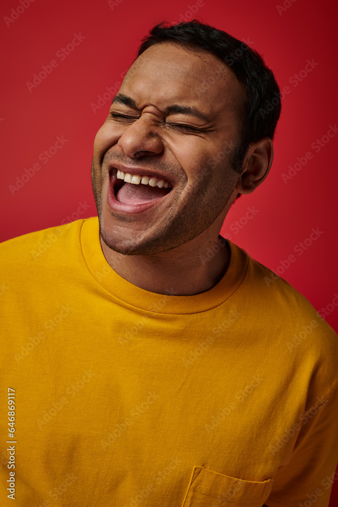 face expression, excited indian man in yellow t-shirt laughing on red background, open mouth face expression, excited indian man in yellow t-shirt laughing on red background, open mouth