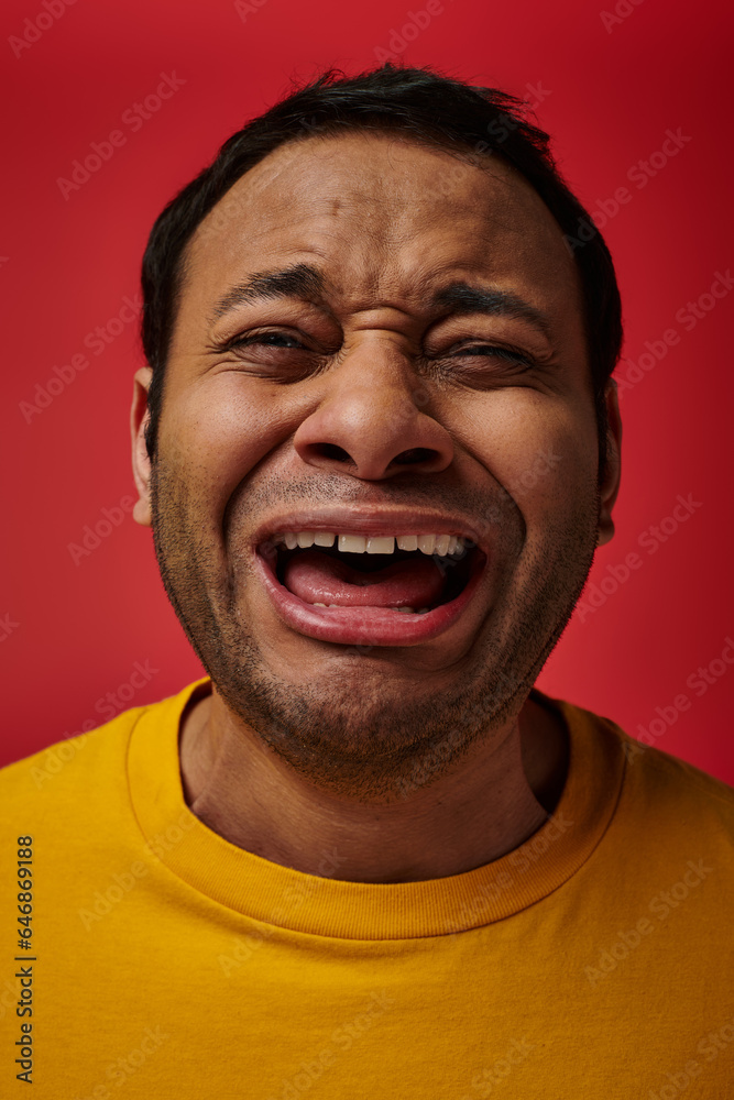 face expression, emotional indian man in yellow t-shirt crying loud on red background, open mouth face expression, emotional indian man in yellow t-shirt crying loud on red background, open mouth