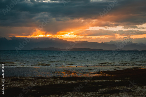 Sunset over Lenin Peak in the Pamir Mountains. On the front lake Karakul. Hard sunset light and gloomy sky.