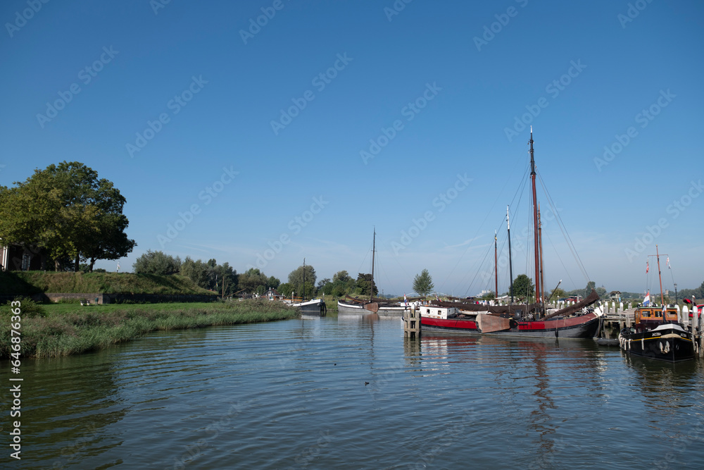 Old sailing boats in the fortified Woudrichem city in The Netherlands, the harbor with a scenic rural typical Dutch landscape and sky in the Waal river on a cold winter day in North Brabant, Europe