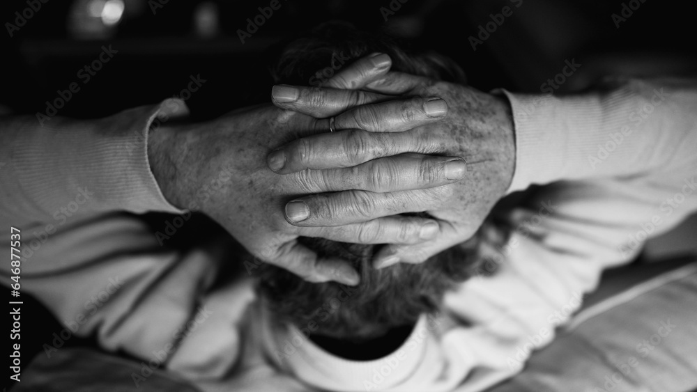 Back of senior man with hands clenched together in pensive mental reflection in monochrome black and white. Pensive elderly man detail hand