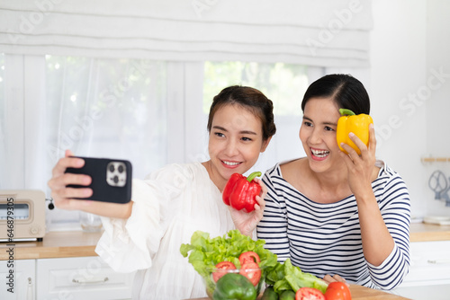 Asian woman girlfriends smiles, holds bell pepper and takes selfies in kitchen