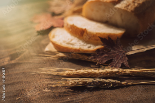 Sliced fresh loaf of bread in paper packaging with ears of wheat and maple leaves on a wooden table.