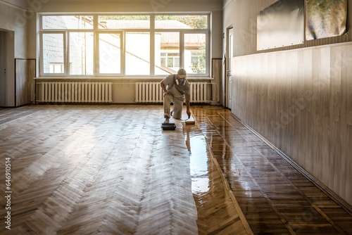Lacquering parquet floors. Professional worker uses a roller to coating floors. Varnish