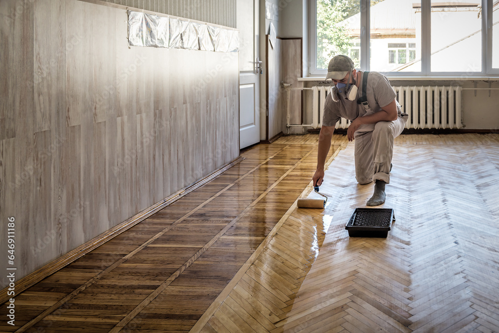 Worker uses a roller to coating floors. Varnishing lacquering parquet floor by paint roller - obrazy, fototapety, plakaty 