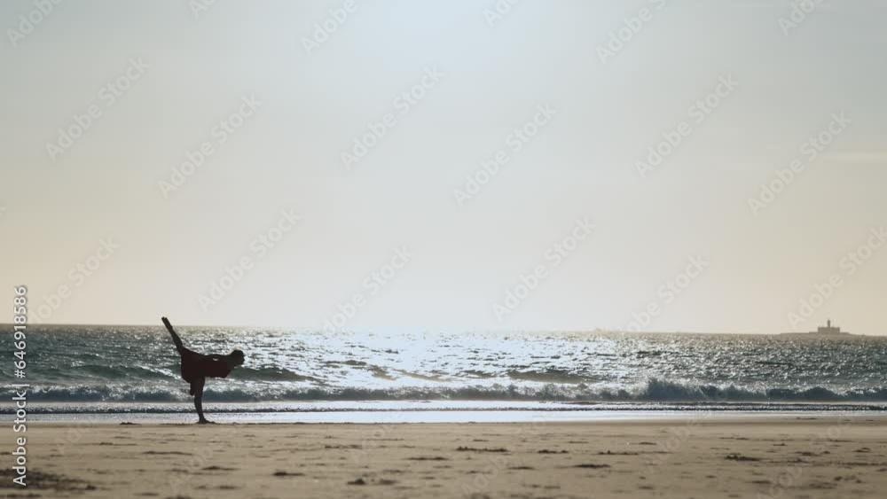 Graceful young woman in a long red dress dancing alone on the beach at early sunset Graceful young woman in a long red dress dancing alone on the beach at early sunset