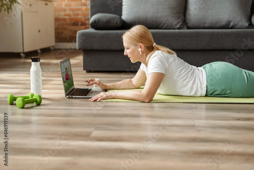 Sport, fitness and healthy lifestyle concept. Senior mature woman exercising on mat at home and using laptop.