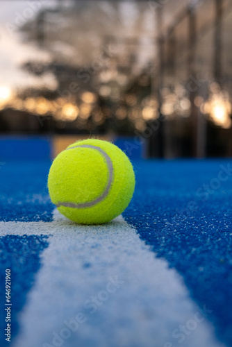 Selective focus. A ball on the line in a blue paddle tennis court at sunset. Racket sports concept © Vic