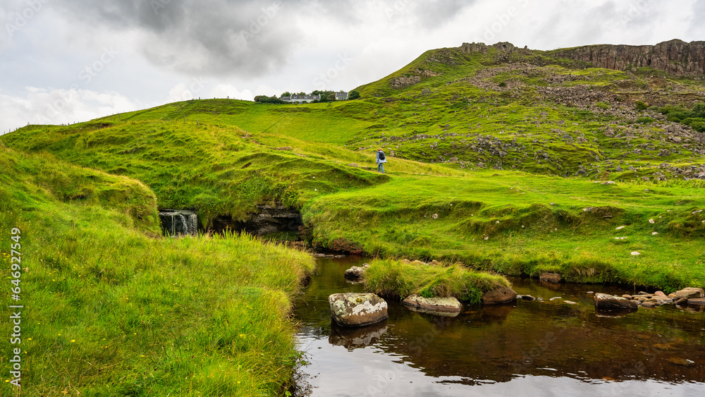 Woman hiking through a green meadow with waterfalls on the Isle of Skye, Scotland. Woman hiking through a green meadow with waterfalls on the Isle of Skye, Scotland.