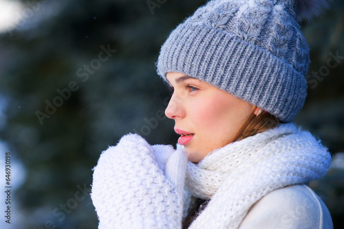 Close up portrait of beautiful young woman at snowy cold winter day in gloves, scarf and knitted hat