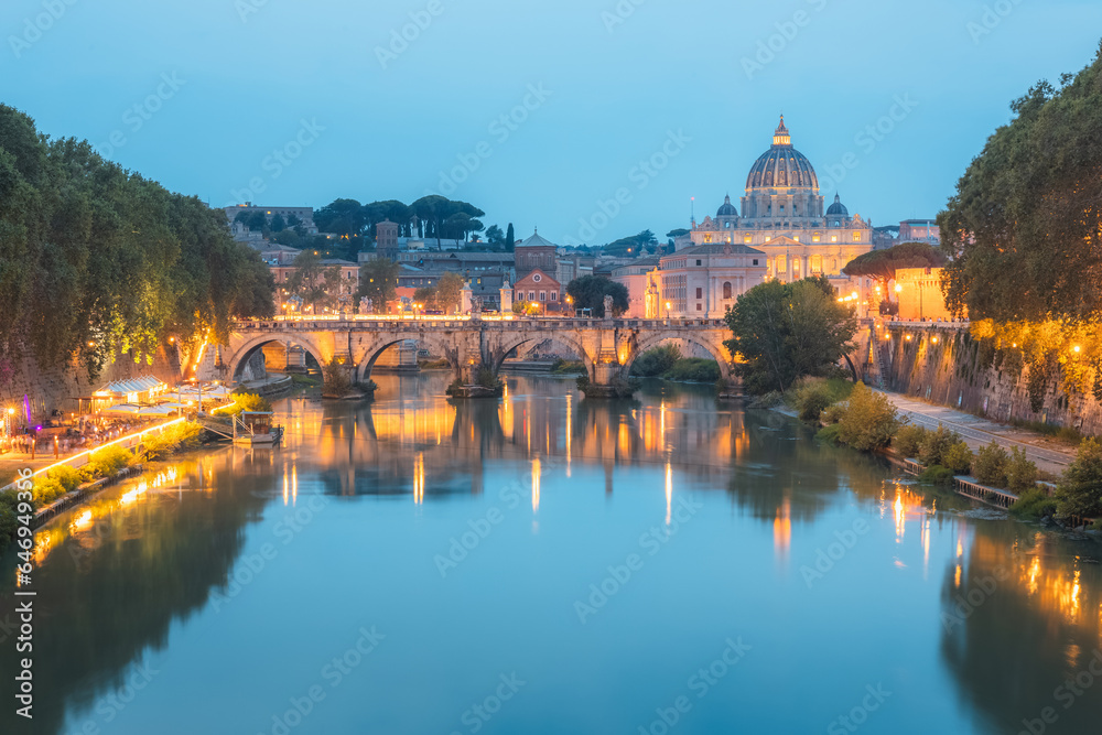 Sceninc twilight view of Saint Peter's Basilica at Vatican City and Ponte Vittorio Emanuele II illuminated along the Tiber River on a summer evening in Rome, Italy.