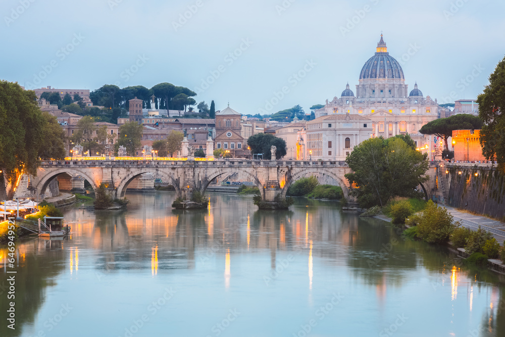 Sceninc twilight view of Saint Peter's Basilica at Vatican City and Ponte Vittorio Emanuele II illuminated along the Tiber River on a summer evening in Rome, Italy.