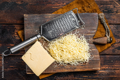 Piece of semi hard cheese and grated cheese with grater. Wooden background. Top view photo