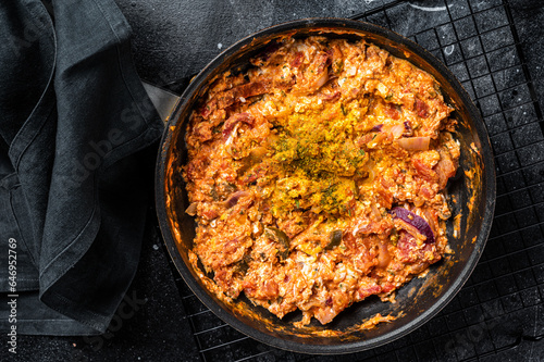 Turkish Menemen omelet in a frying pan. Black background. Top view