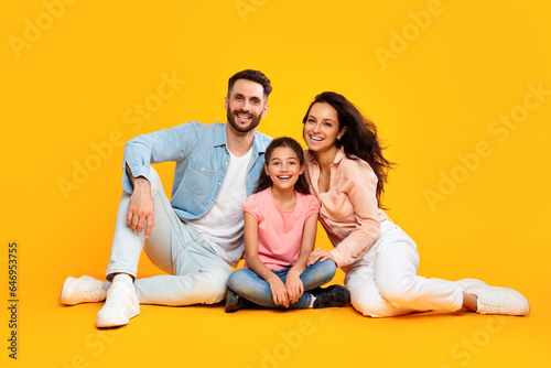 Parenthood and childhood concept. Happy caucasian parents mom and dad sitting on floor with daughter, yellow background