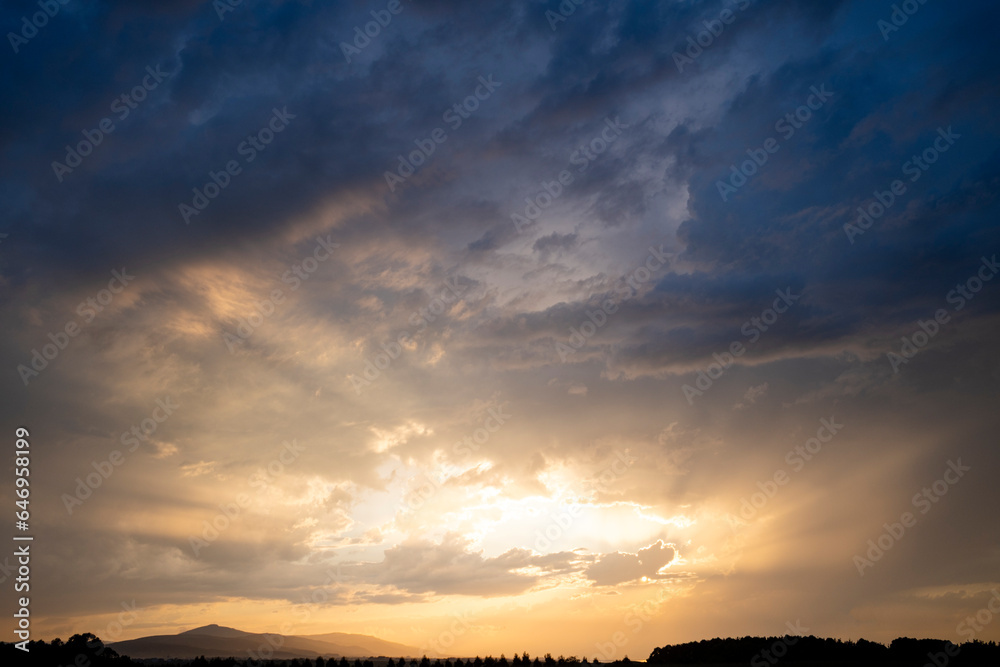 View of a cloudscape at sunset over the horizon, in warm blue tones.