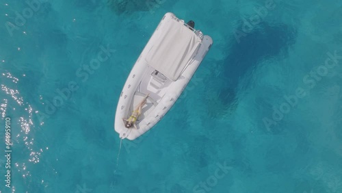 Girl sunbathing on a boat in the crystal clear sea, aerial top down view, Sardinia, Italy