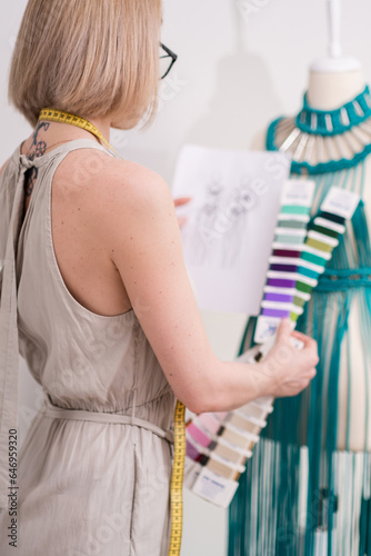 Designer with color palette and sketch stands by green macrame dress on mannequin in sewing workshop creative lady dressmaker creates stylish women clothes in studio