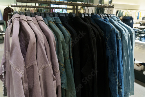 Denim shirts with long sleeves hang on hangers in a clothing store.
