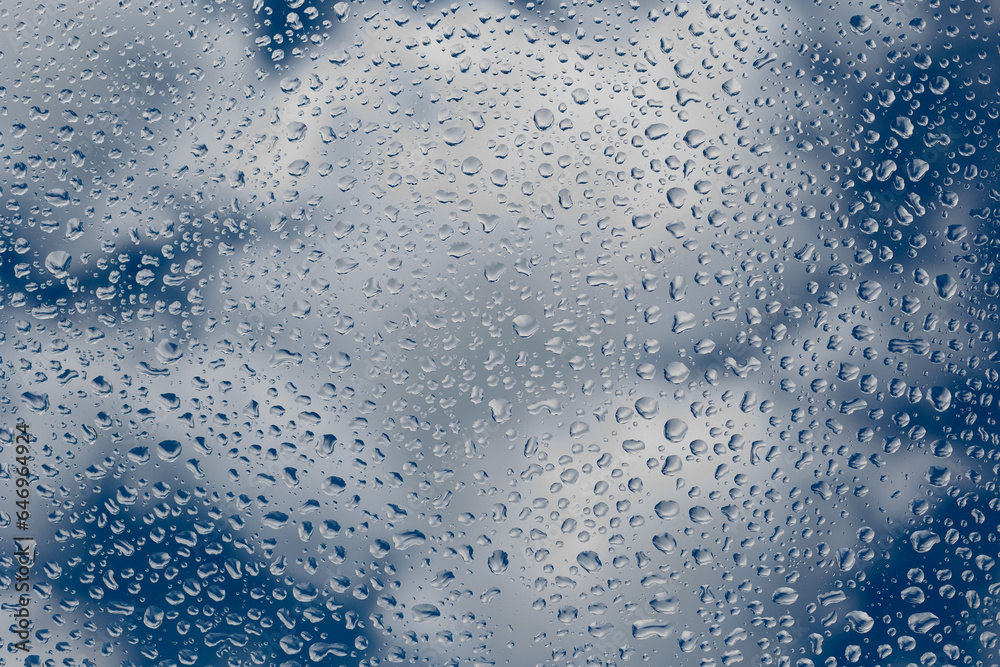 Raindrops on the glass on the background of a blue cloudy sky.