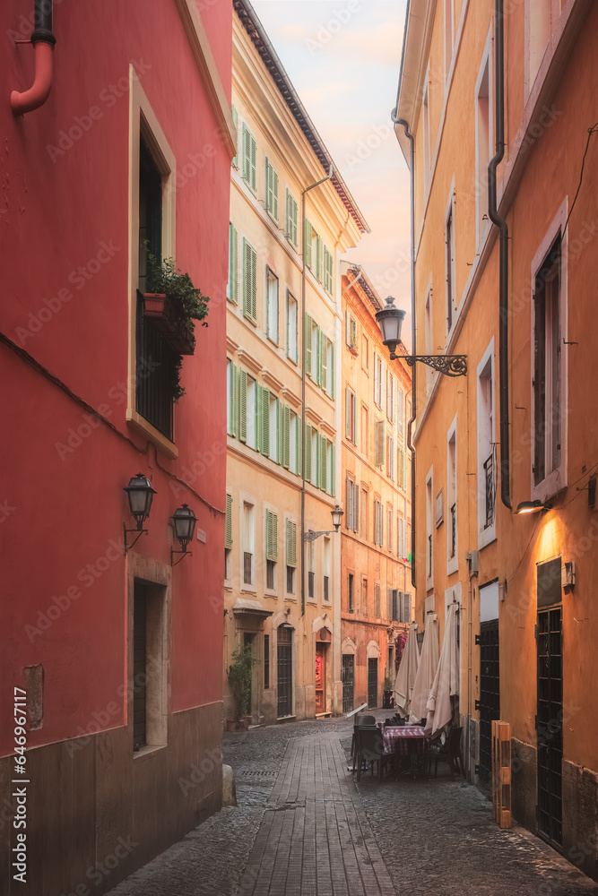 Bright, colourful residential buildings and architecture along a quiet, narrow cobblestone lane in Rione VI Parione in the old town of historic central Rome, Italy.