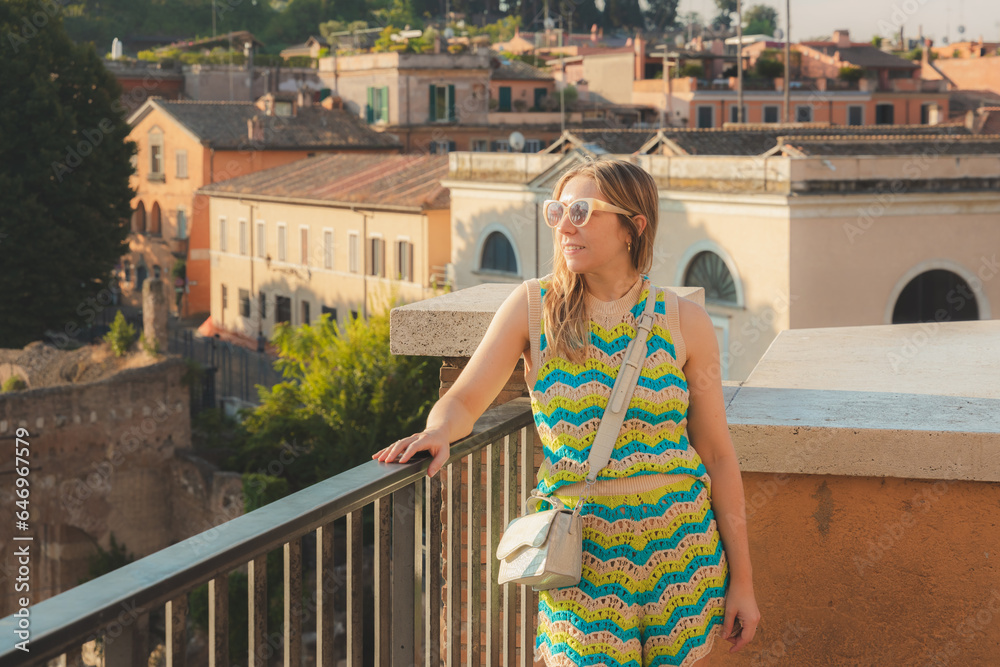 A young, blonde female tourist enjoys the views over the ancient classical ruins of the historic Roman Forum as seen from Capitoline Hill or Campidoglio in Rome, Italy.