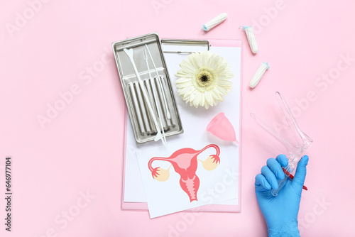 Hand in medical glove, with gynecological speculum, pap smear test tools, drawing of female uterus, menstrual cup and tampons on pink background © Pixel-Shot