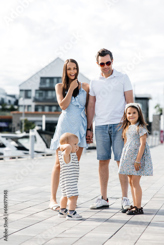 A young family of four is walking on the street. Mom and dad together with their little son and daughter. Happy family spends leisure time outdoors. Family having fun