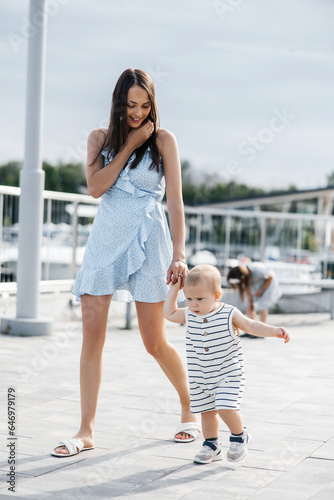 Mom and her little son are walking in the fresh air. Walk of a young mother and her little son. Mom is wearing a summer dress, and her son is wearing a striped suit. Mom smiles and enjoys the walk
