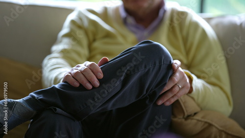 Senior man with legs crossed, detail close-up of older person seated on couch sofa at home wearing yellow sweater and pants © Marco