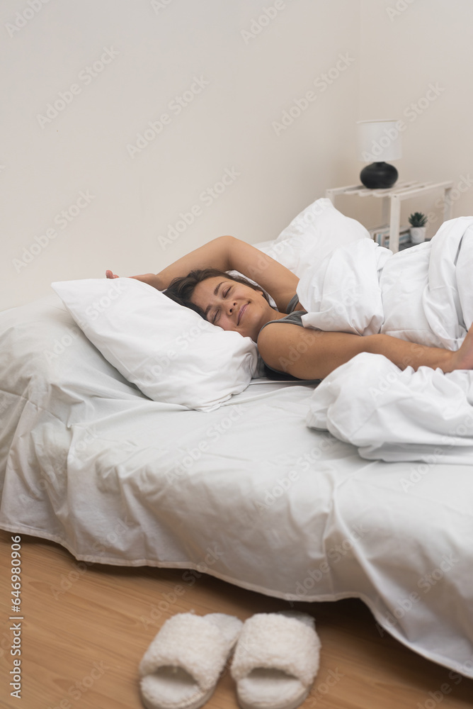 Woman in nightgown sleeps in comfortable position on bed with light pastels in bedroom with potted plant in apartment lady rests getting energy from sleeping Woman in nightgown sleeps in comfortable position on bed with light pastels in bedroom with potted plant in apartment lady rests getting energy from sleeping