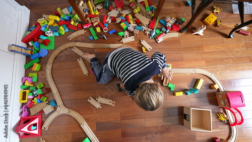 Small boy playing with toys seen from above perspective, child immersed in play with retro vintage railroad tracks and blocks scattered around photo