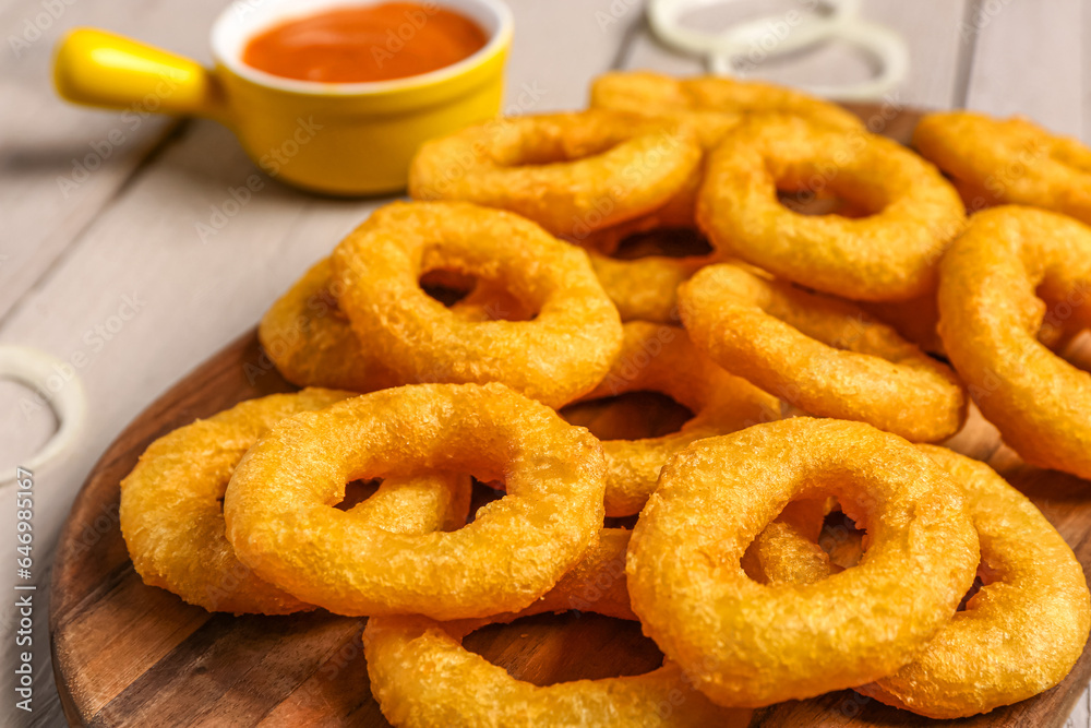 Board with fried breaded onion rings and sauce on grey wooden background, closeup