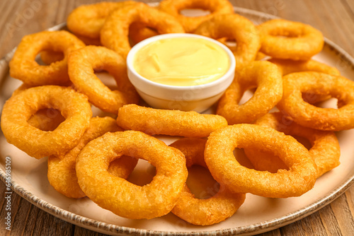 Plate with fried breaded onion rings and mayonnaise on wooden background, closeup
