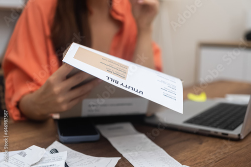 woman examines utility bills closely, wrestling with the escalating expenses of electricity, water, and internet services photo