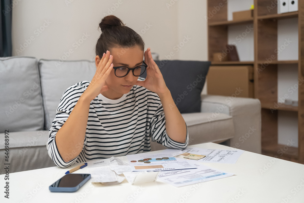 Budget Distress: Stressed by debt, a woman manages household finances, calculates expenses, and seeks solace in online payments while feeling unhappy. Budget Distress: Stressed by debt, a woman manages household finances, calculates expenses, and seeks solace in online payments while feeling unhappy.