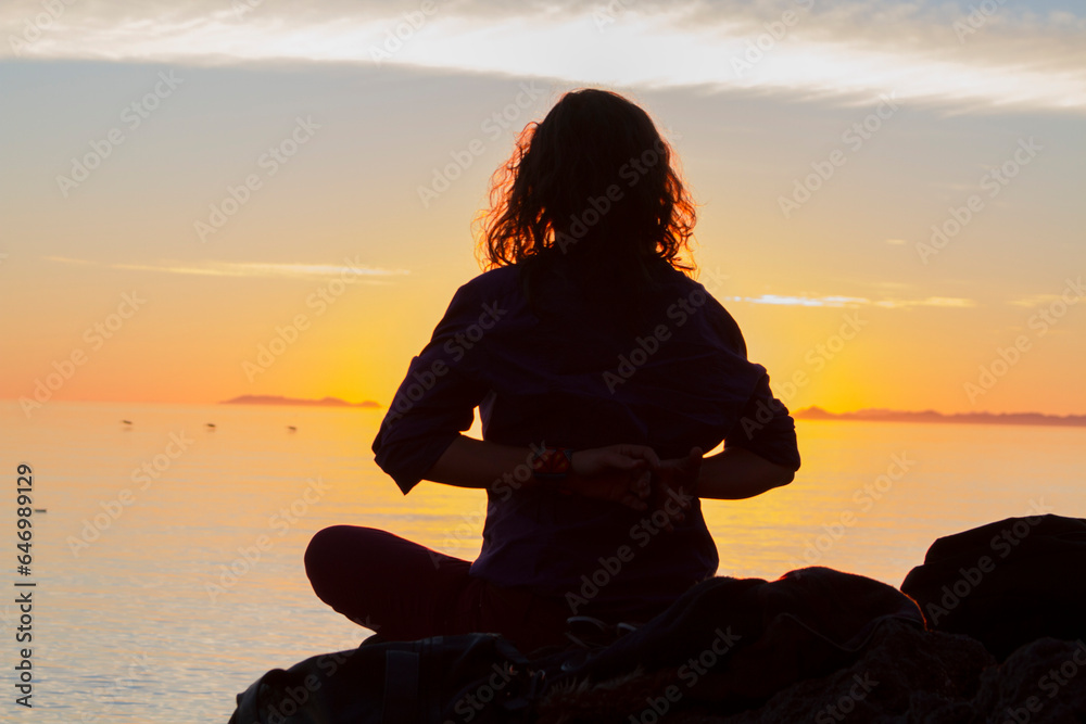 Silueta de mujer meditando a la orilla del mar durante el atardecer