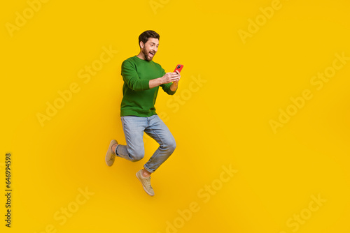 Full size body photo of screaming crazy guy shopaholic surprised holding smartphone jump trampoline isolated on yellow color background