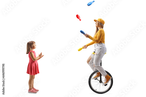 Little girl watching a young female riding a unicycle and juggling