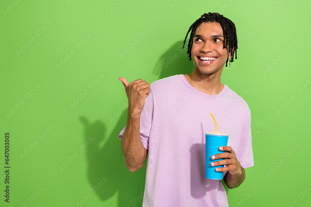 Portrait of funky handsome guy hold soda drink cup look indicate finger empty space isolated on green color background Portrait of funky handsome guy hold soda drink cup look indicate finger empty space isolated on green color background